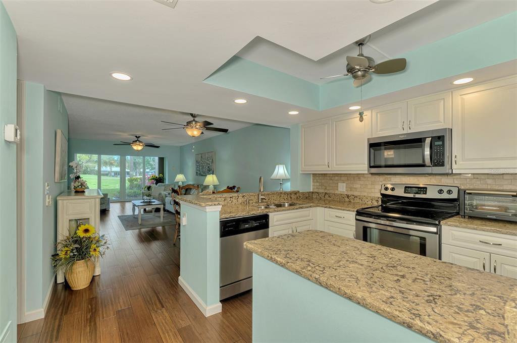 A kitchen with granite countertops and white cabinets overlooks an open-concept living area — 433 CERROMAR LANE UNIT 341, VENICE, FL