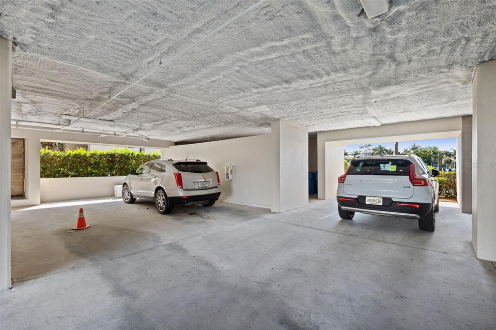 A covered parking garage features concrete ceilings, white walls, and two parked SUVs — 2775 KIPPS COLONY DRIVE S UNIT 305, GULFPORT, FL