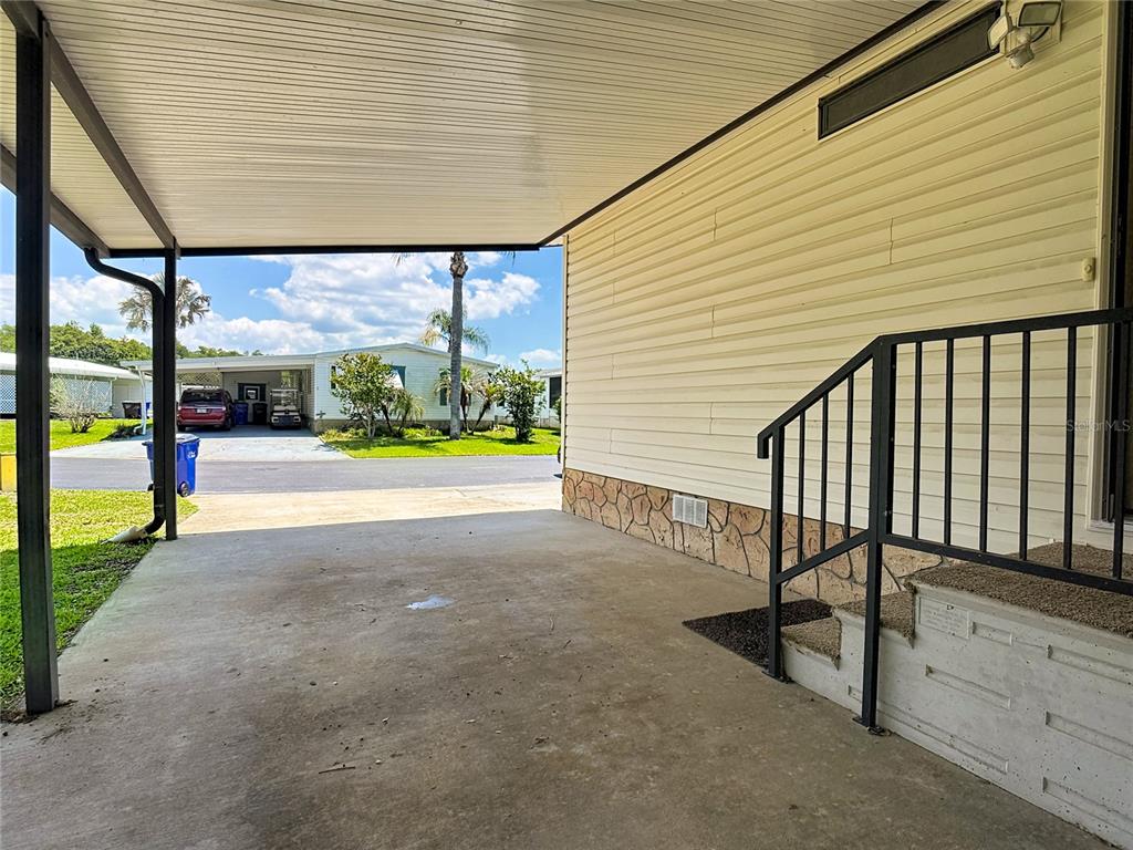 A covered concrete carport sits beside a mobile home with light siding and stone skirting — 4424 BRAVE LANE, ST CLOUD, FL