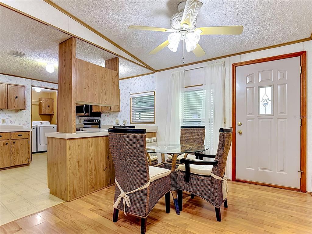 A dining area with a glass table and wicker chairs next to a wood-paneled kitchen — 4424 BRAVE LANE, ST CLOUD, FL
