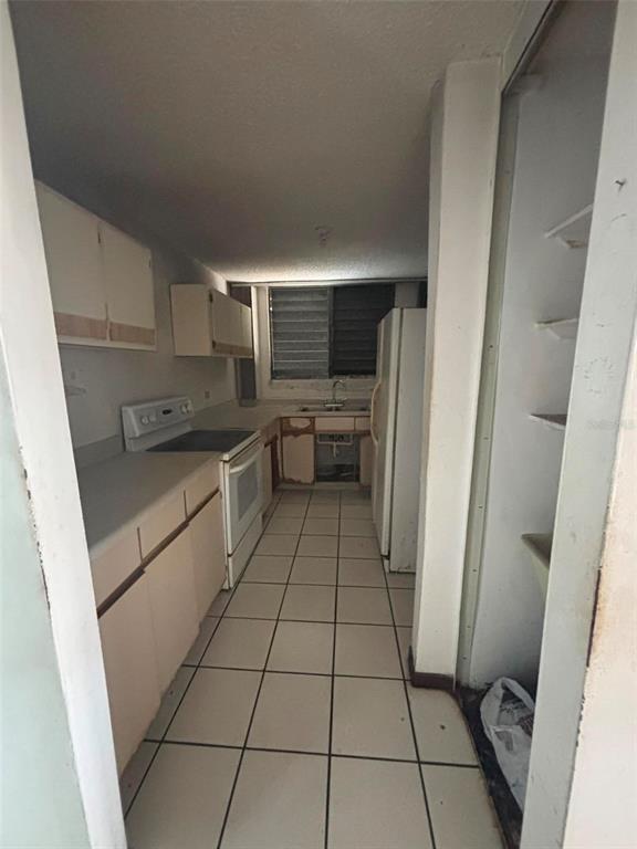 A galley kitchen features white cabinets, a white stove, and light-colored floor tiles — 81 Mayaguez Street Apt 32 CONDO FRENCH PLAZA UNIT 327, SAN JUAN, PR