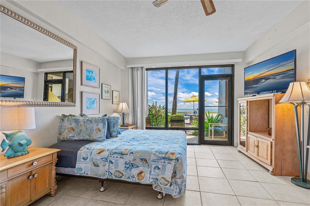 A bedroom with tile floors, a bed with coastal bedding, and a view of the beach — 2301 S ATLANTIC AVENUE UNIT 120, DAYTONA BEACH SHORES, FL