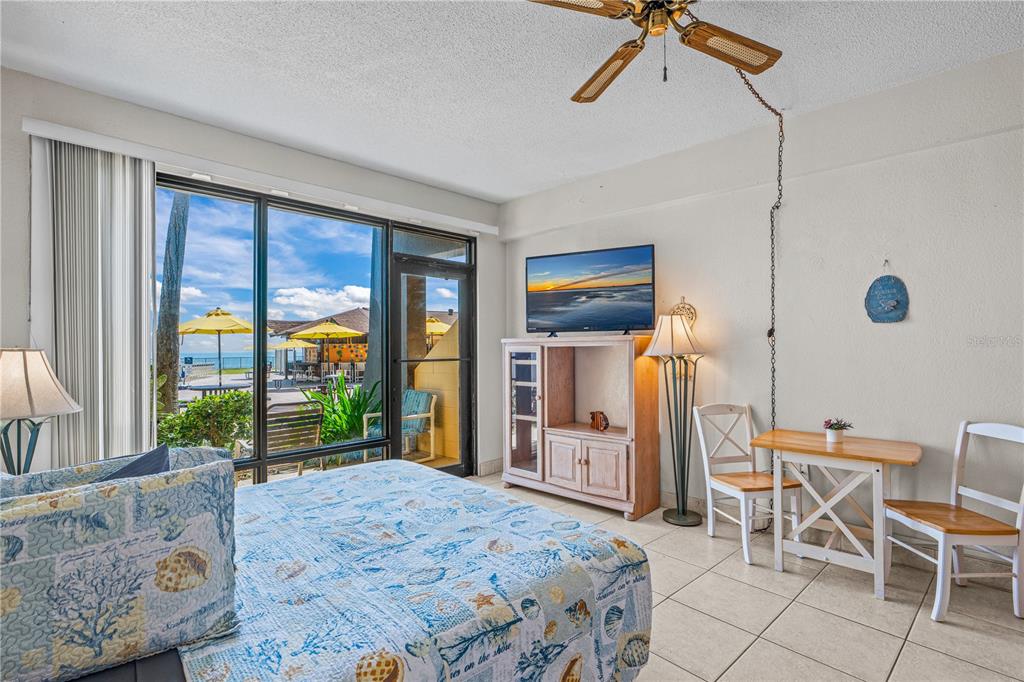 A bedroom with a bed, television, dining set, and a large window overlooking a beach — 2301 S ATLANTIC AVENUE UNIT 120, DAYTONA BEACH SHORES, FL