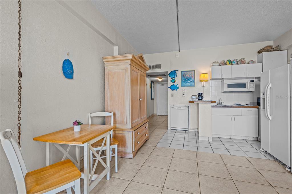 A dining area with a wooden table sits adjacent to a white kitchen — 2301 S ATLANTIC AVENUE UNIT 120, DAYTONA BEACH SHORES, FL