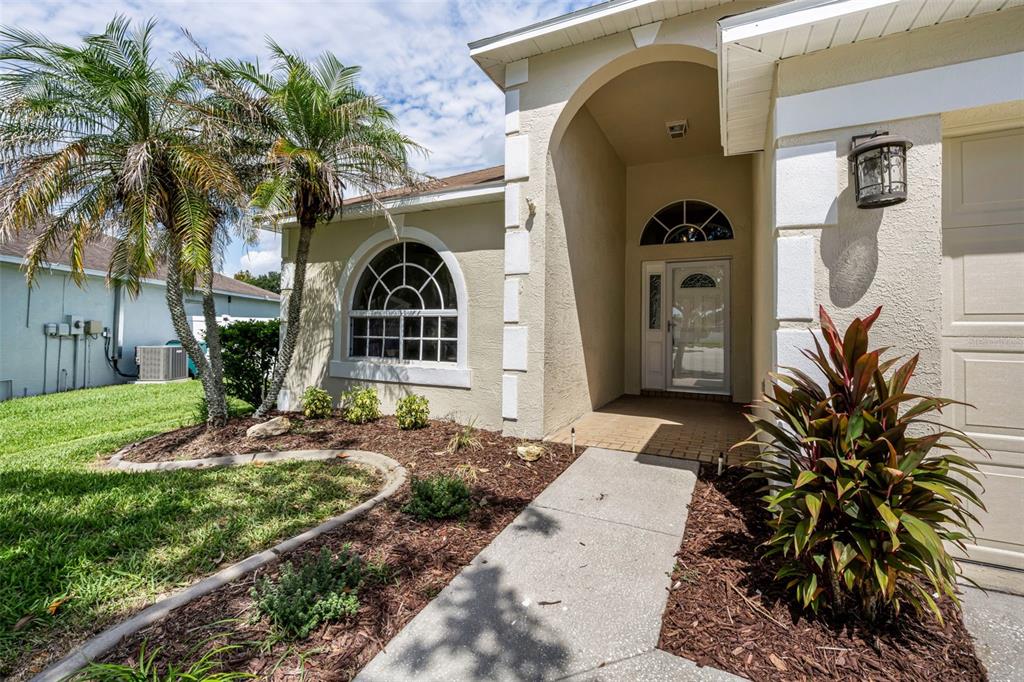 The exterior of a beige house features a arched entryway, a palm tree, and landscaping — 25427 SEVEN RIVERS CIRCLE, LAND O LAKES, FL