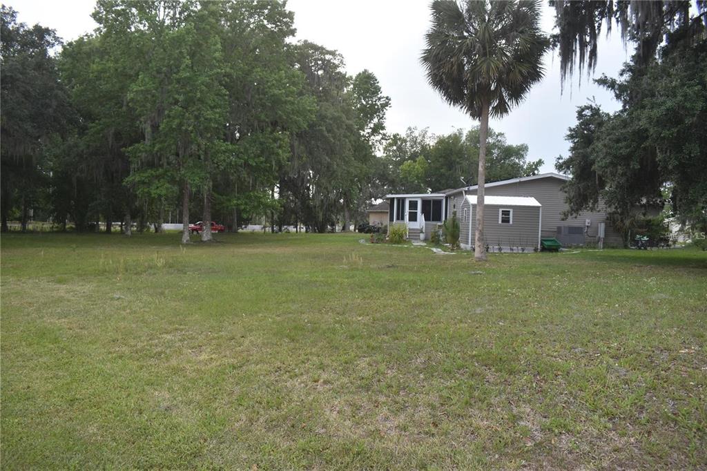A large grassy yard leads to a single-story house with a palm tree and shed — LOT 12 BLK D LEXINGTON CIR COURT, WILDWOOD, FL