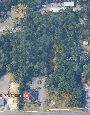This aerial view shows a commercial building with a parking lot and a large wooded lot — 2275 N VOLUSIA AVENUE, ORANGE CITY, FL