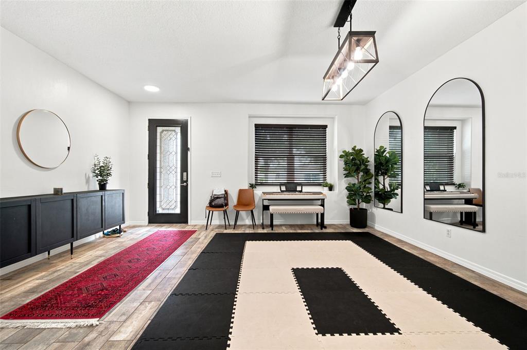 A bright room features white walls, wood-look flooring, a black console, and a workout mat — 428 CHIMNEY ROCK DRIVE, RUSKIN, FL