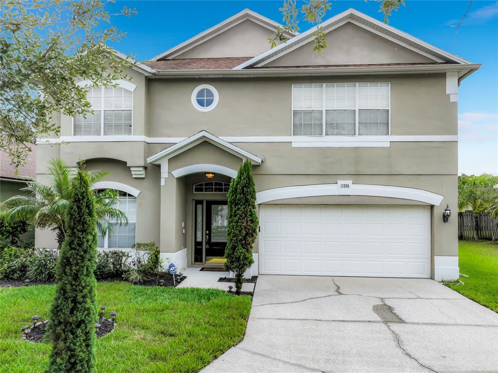 A two-story suburban house with a beige stucco exterior, a two-car garage, and a driveway — 13556 HAWKEYE DRIVE, ORLANDO, FL