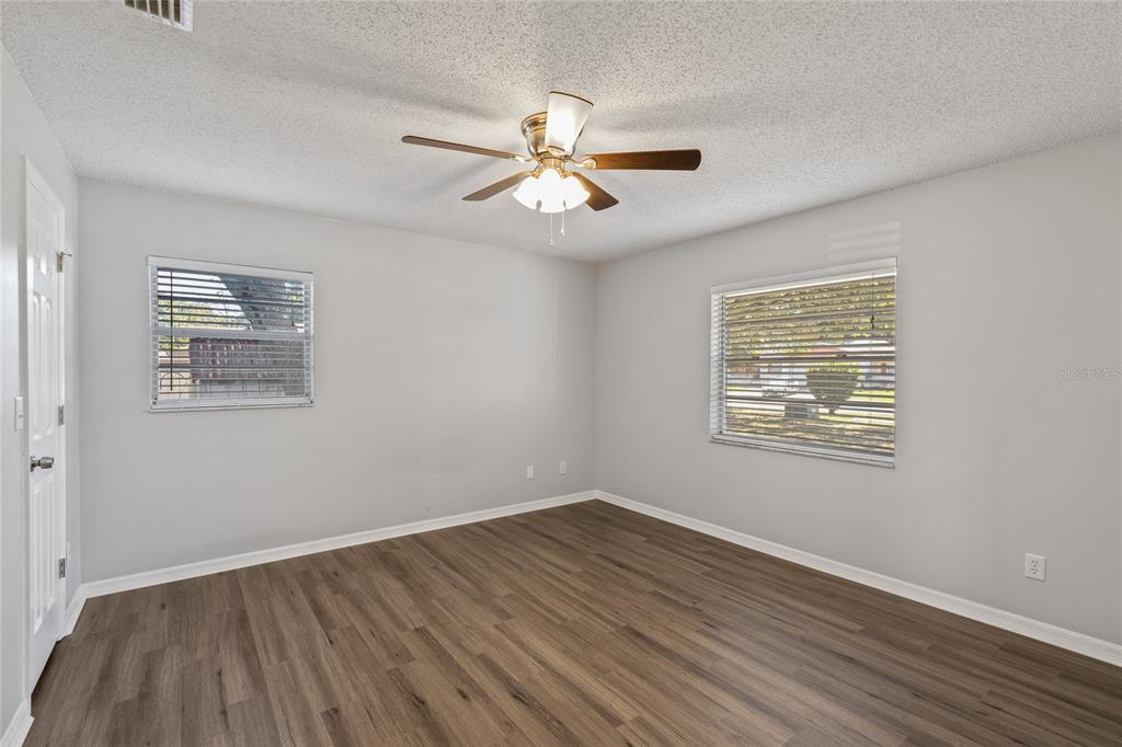 An empty bedroom features light gray walls, wood-look flooring, two windows, and a ceiling fan — 2711 N DELLWOOD DRIVE, EUSTIS, FL