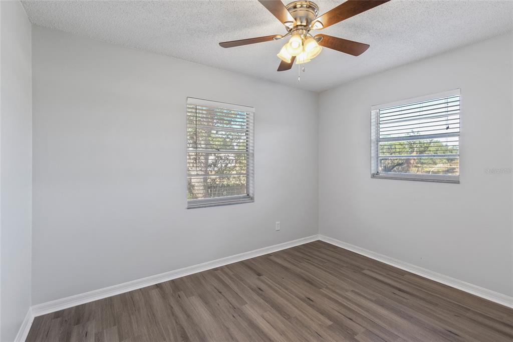 An empty bedroom features light gray walls, wood-look flooring, a ceiling fan, and two windows — 2711 N DELLWOOD DRIVE, EUSTIS, FL