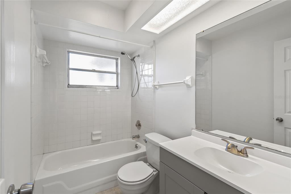 A bathroom features a white bathtub, a toilet, and a gray vanity with a mirror — 2711 N DELLWOOD DRIVE, EUSTIS, FL