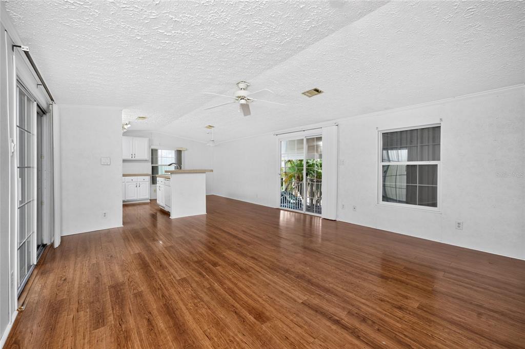 An open-concept living area with wood-look flooring, white walls, a ceiling fan, and a kitchen — 10 HOLLAND DRIVE, PUNTA GORDA, FL