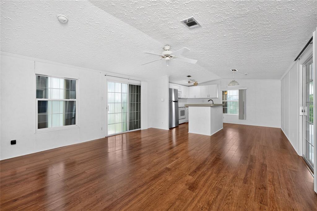 An open-concept living area with wood-look flooring, white walls, a ceiling fan, and kitchen — 10 HOLLAND DRIVE, PUNTA GORDA, FL