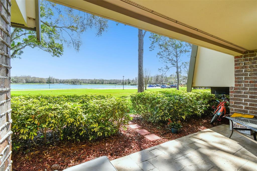 A covered patio overlooks a grassy lawn, a lake, and trees under a clear sky — 36750 US HIGHWAY 19 N UNIT 04138, PALM HARBOR, FL