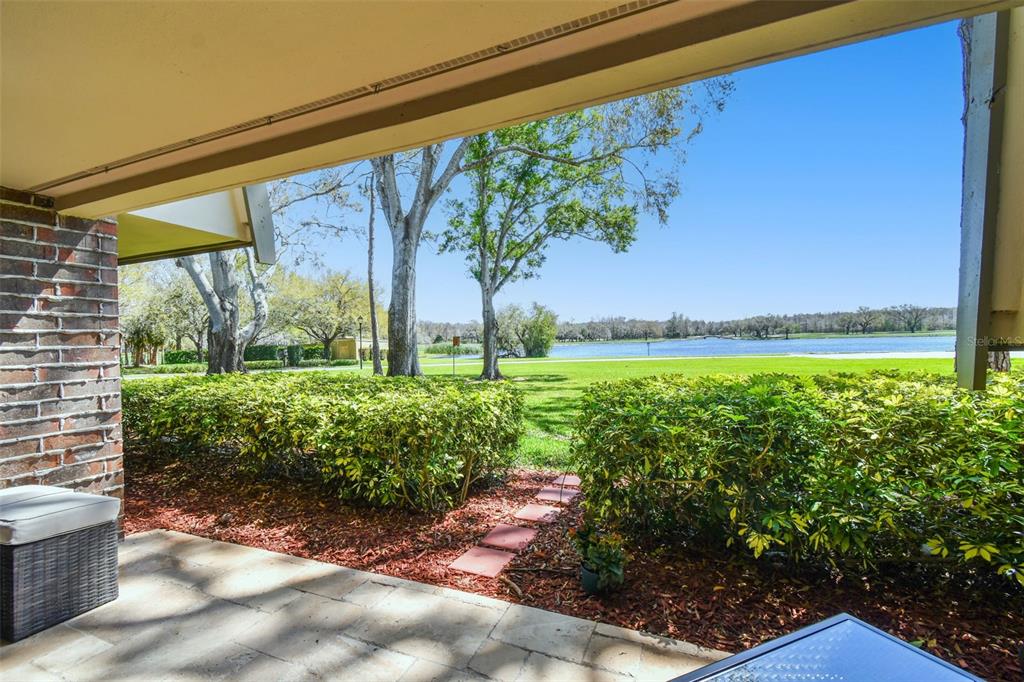 A covered patio overlooks a landscaped lawn, trees, and a lake on a sunny day — 36750 US HIGHWAY 19 N UNIT 04138, PALM HARBOR, FL
