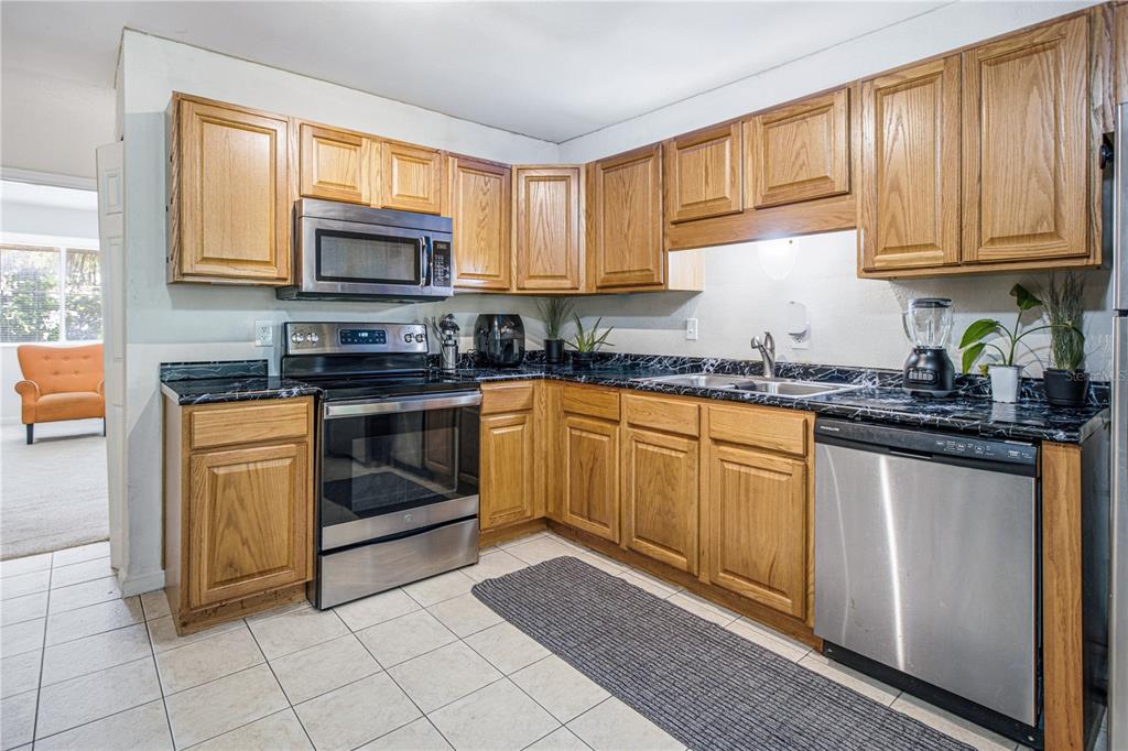 A kitchen features wood cabinets, black marble-patterned countertops, and stainless steel appliances — 8880 OLD KINGS ROAD S UNIT 4, JACKSONVILLE, FL