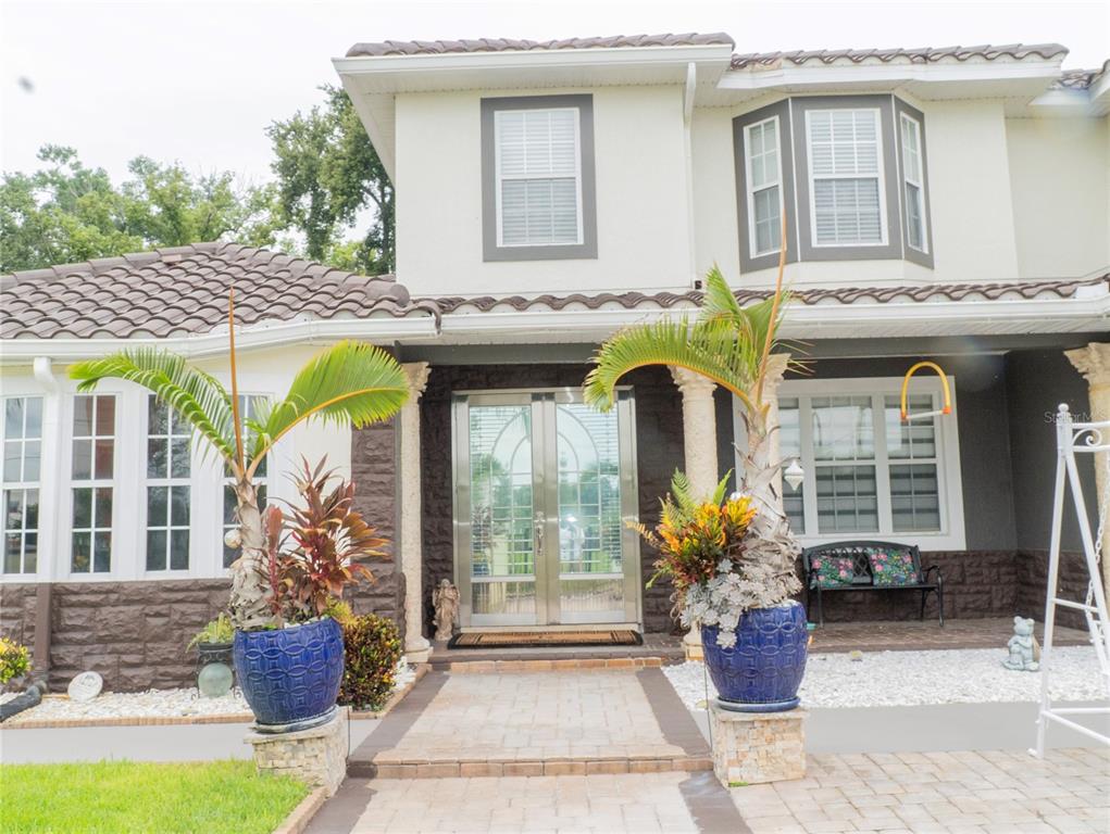 A two-story house exterior features a stone facade, double glass doors, and two potted palms — 1304 OCOEE APOPKA ROAD, OCOEE, FL