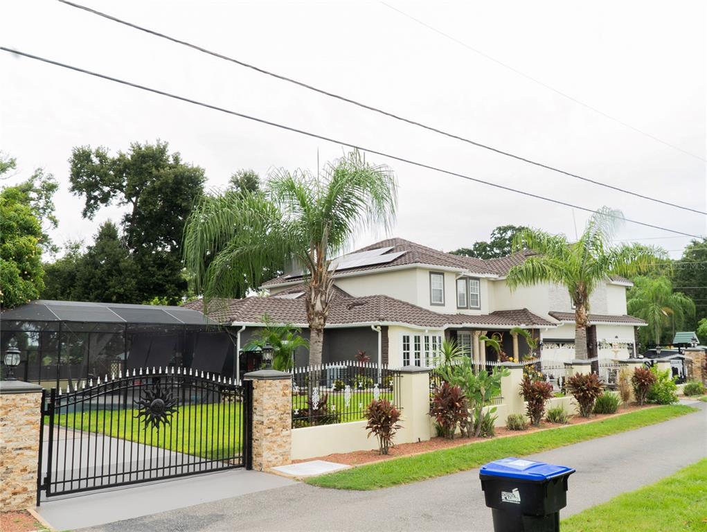 A two-story house with a tiled roof, solar panels, and a gated yard with palm trees — 1304 OCOEE APOPKA ROAD, OCOEE, FL