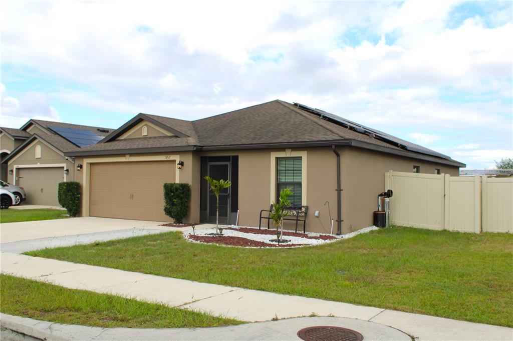 A single-story house with a tan stucco exterior, a two-car garage, and solar roof panels — 1552 SWAN LAKE CIRCLE, DUNDEE, FL