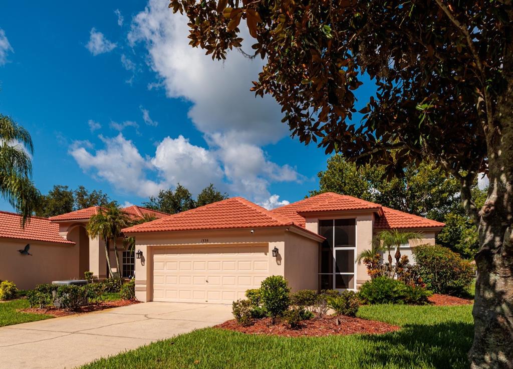 A brick wall with a Crescent Oaks sign sits behind a colorful flower garden — 1338 DARTFORD DRIVE, TARPON SPRINGS, FL