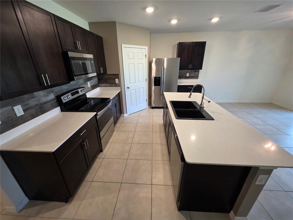 A kitchen features dark wood cabinets, white countertops, stainless steel appliances, and a central island — 27441 NATAL DRIVE, PUNTA GORDA, FL