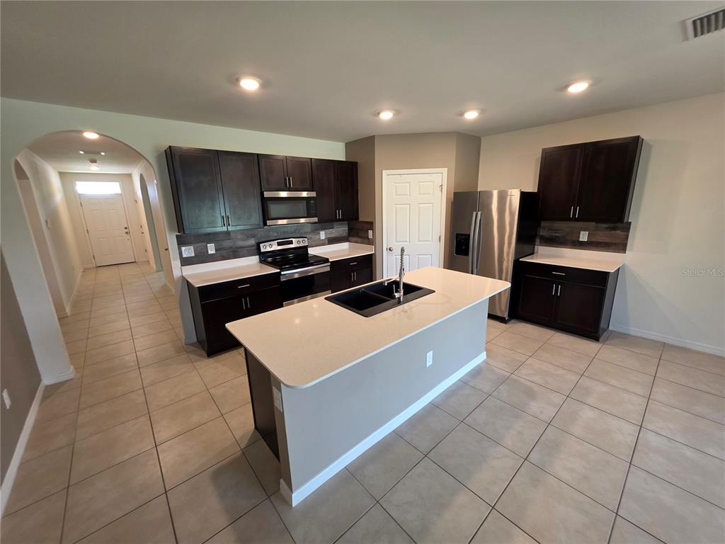 A kitchen features dark wood cabinets, stainless steel appliances, a central island, and tile flooring — 27441 NATAL DRIVE, PUNTA GORDA, FL