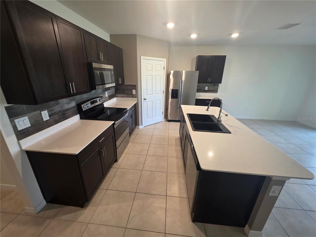 A kitchen features dark wood cabinets, white countertops, stainless steel appliances, and a central island — 27441 NATAL DRIVE, PUNTA GORDA, FL