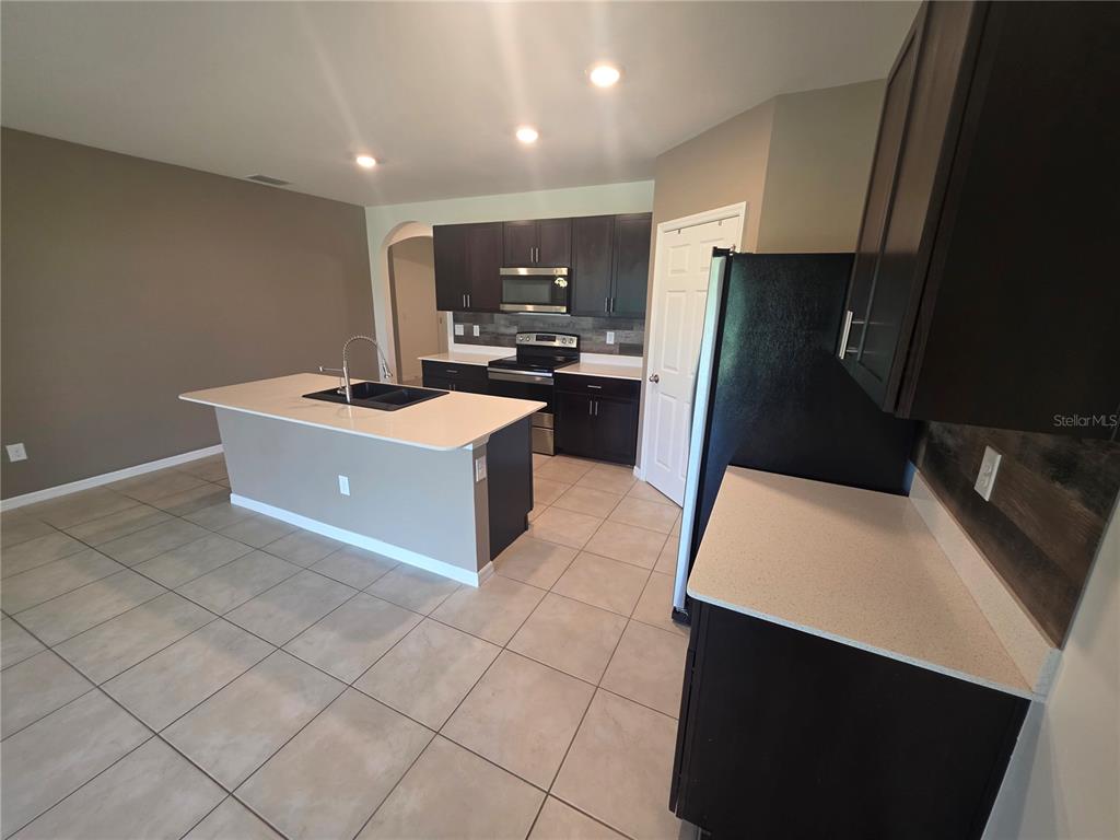 A kitchen features dark wood cabinets, light countertops, a center island, and tile flooring — 27441 NATAL DRIVE, PUNTA GORDA, FL