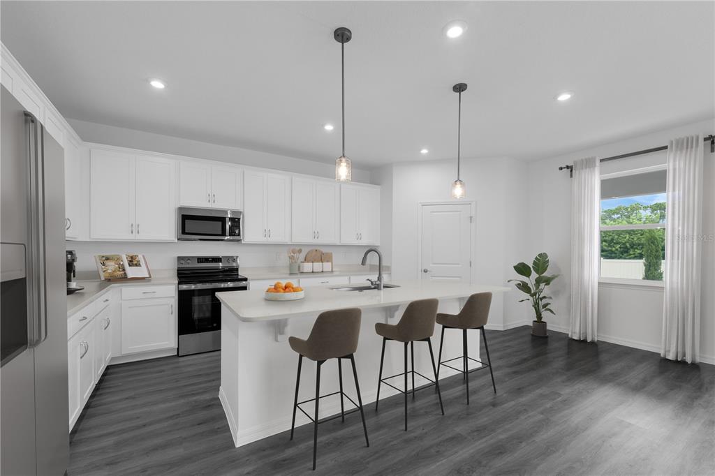 A modern kitchen features white cabinets, a central island with bar stools, and dark flooring — 10141 HUNTINGNET WAY, LEESBURG, FL