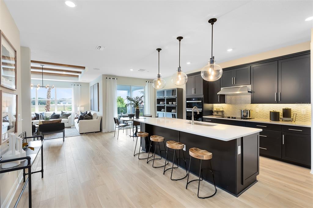 A modern open-concept kitchen features dark cabinetry, a white island with barstools, and light flooring — 5513 SETTLINGSTONE LANE, ST CLOUD, FL
