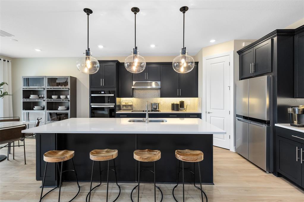 A modern kitchen features black cabinetry, a white island with bar stools, and stainless appliances — 5513 SETTLINGSTONE LANE, ST CLOUD, FL