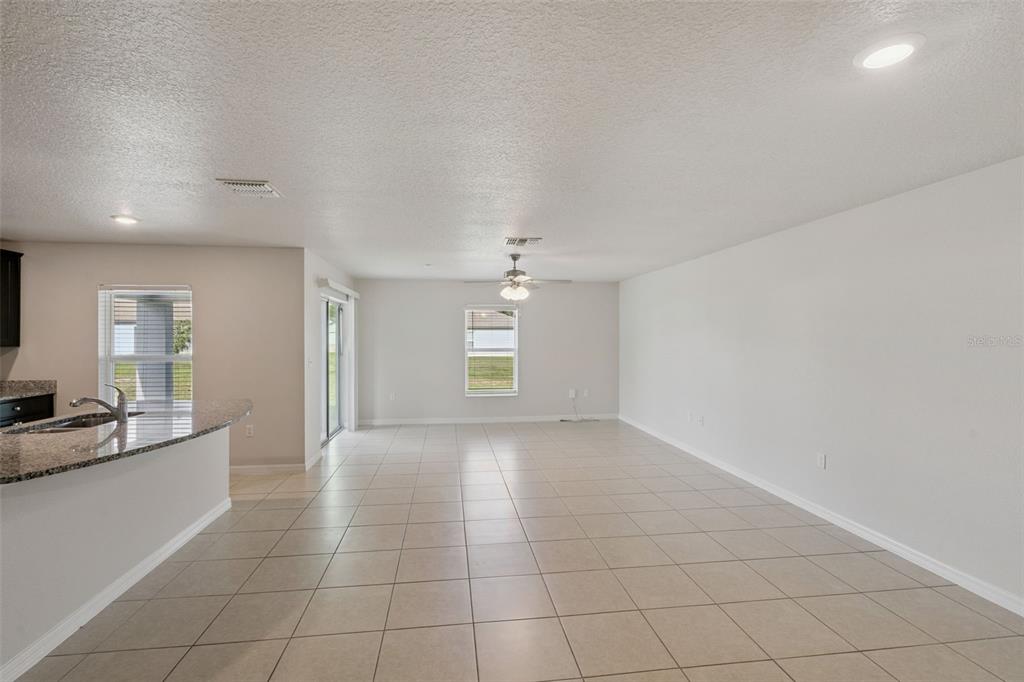 An open-concept living area features light-colored tile flooring, a ceiling fan, and a kitchen counter — 1350 BRENWAY DRIVE, MASCOTTE, FL