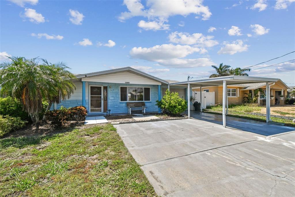 A single-story house with a blue facade, a front porch, and an attached metal carport — 13603 ALLYN DRIVE, HUDSON, FL