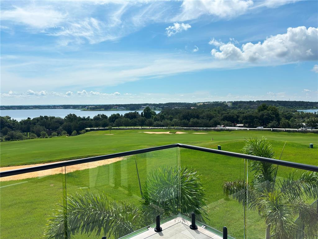 A balcony with a glass railing overlooks a golf course, trees, and a distant lake — 16142 TRIVOLI CIRCLE, MONTVERDE, FL