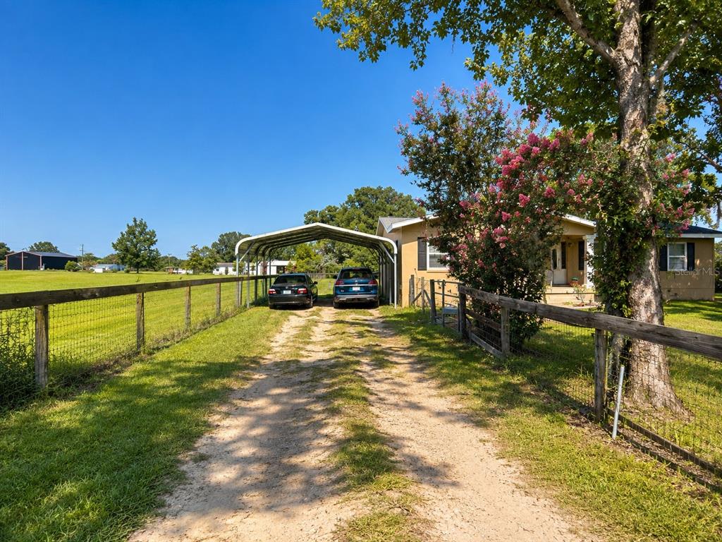 A dirt driveway leads to a metal carport and a house with a fenced yard — 9390 NE 16TH TERRACE, ANTHONY, FL