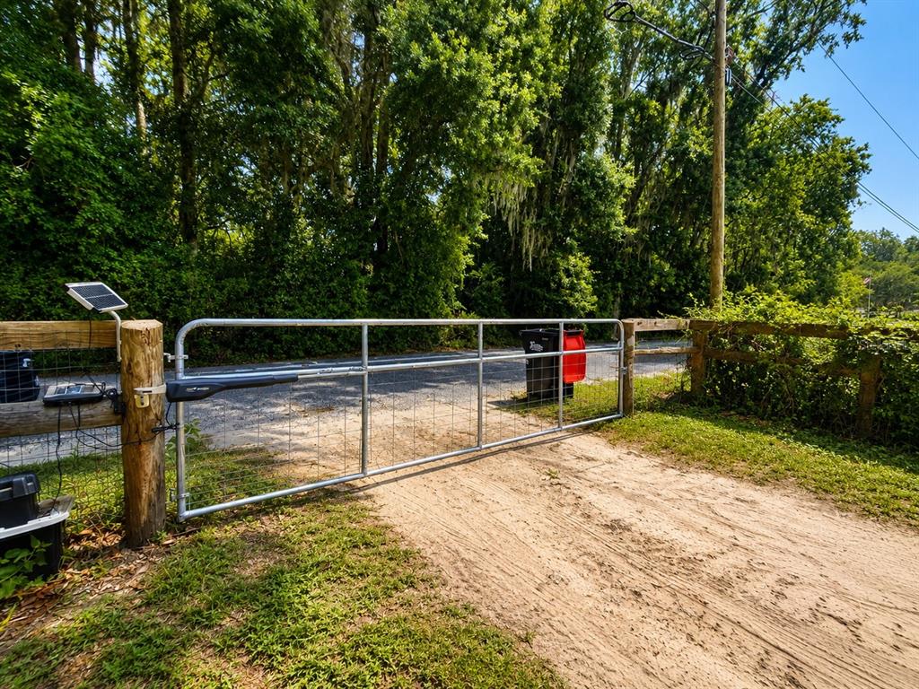 A metal gate with an automatic opener stands at the entrance of a dirt driveway — 9390 NE 16TH TERRACE, ANTHONY, FL