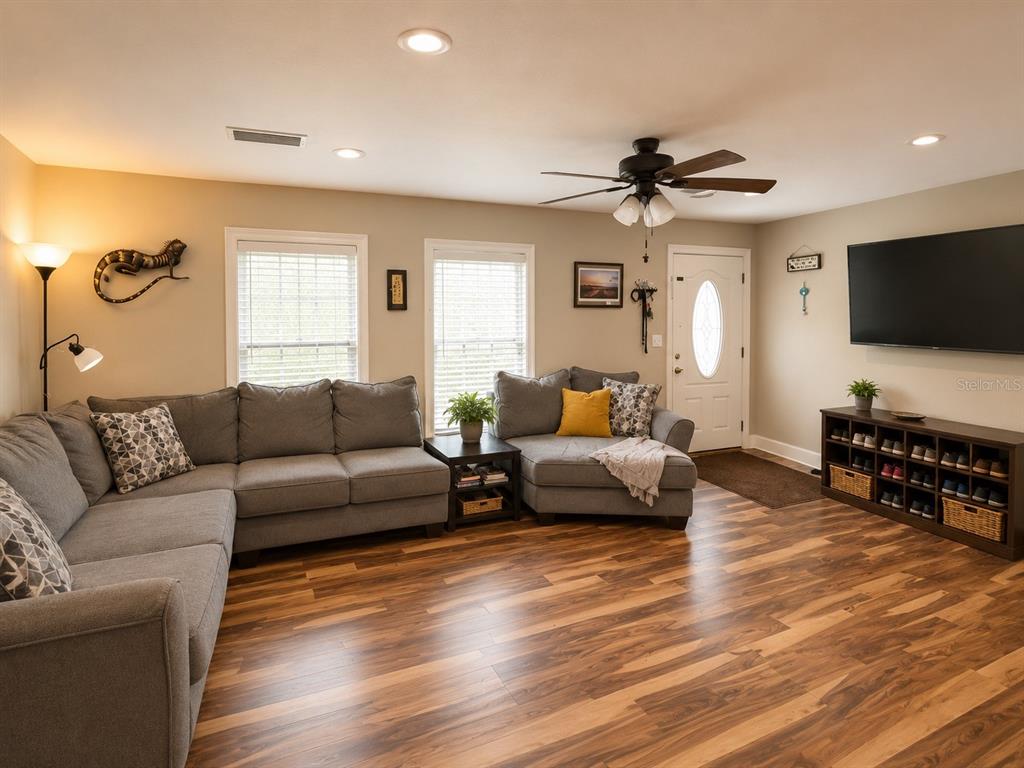 A living room features a gray sectional sofa, wood-look flooring, and a wall-mounted television — 9390 NE 16TH TERRACE, ANTHONY, FL