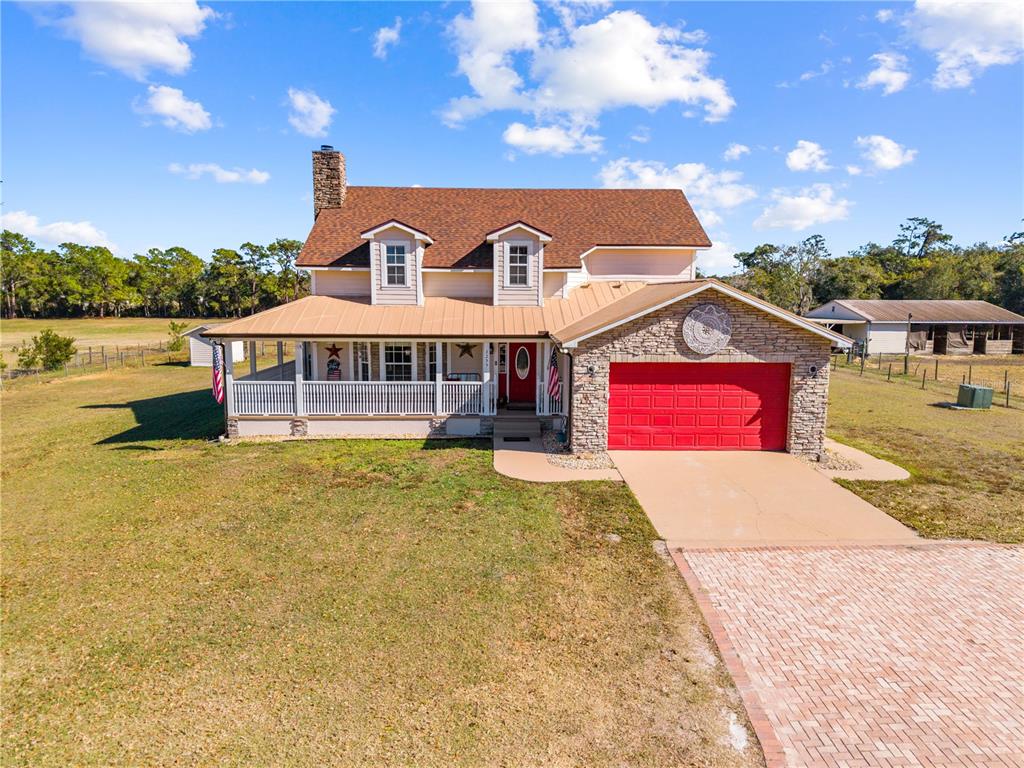 A two-story house with a metal-roofed porch, stone accents, and a red garage door — 3255 TUCKER AVENUE, ST CLOUD, FL