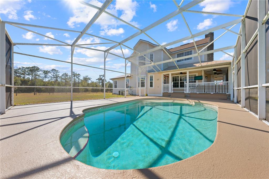 A swimming pool sits inside a screened-in patio behind a two-story house with a yard — 3255 TUCKER AVENUE, ST CLOUD, FL
