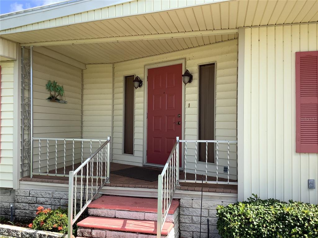 A red front door with side windows sits on a porch with metal railings — 269 SALEM AVENUE UNIT 9, PALM HARBOR, FL