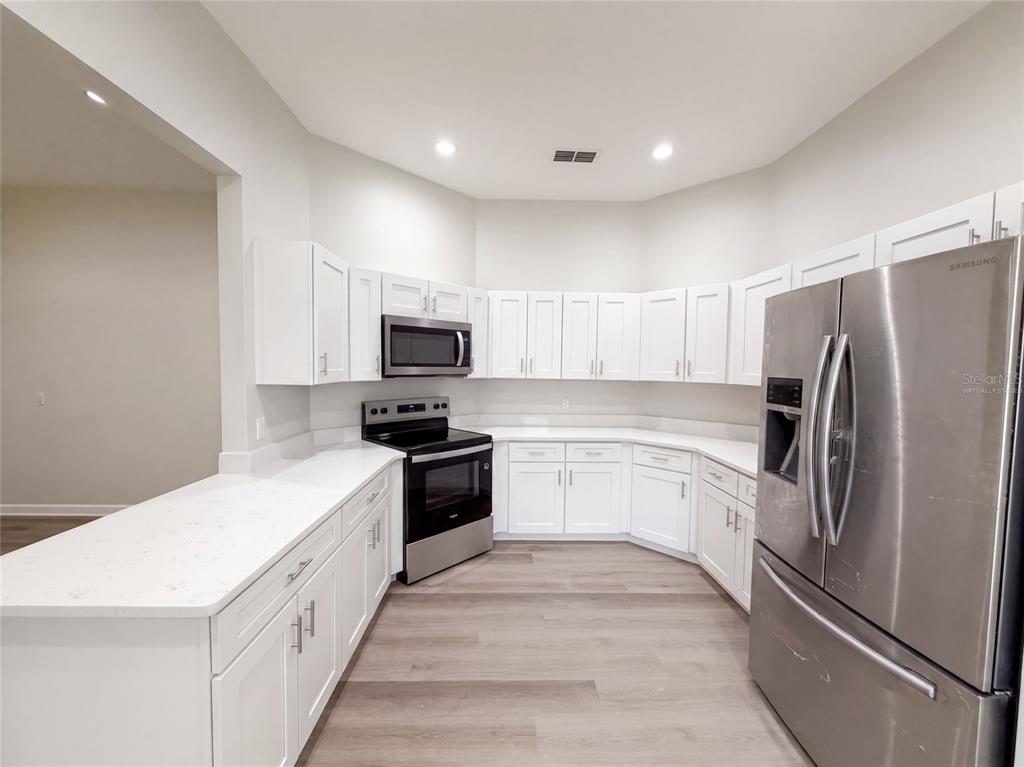 A kitchen features white cabinets, stainless steel appliances, and light-colored countertops over wood-look flooring — 24 BAY POINTE DRIVE, ORMOND BEACH, FL