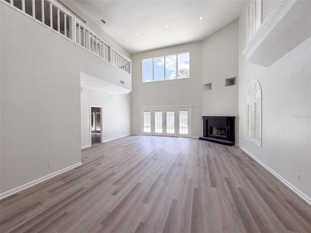 A spacious living room features high ceilings, light wood-look flooring, a fireplace, and a balcony — 24 BAY POINTE DRIVE, ORMOND BEACH, FL