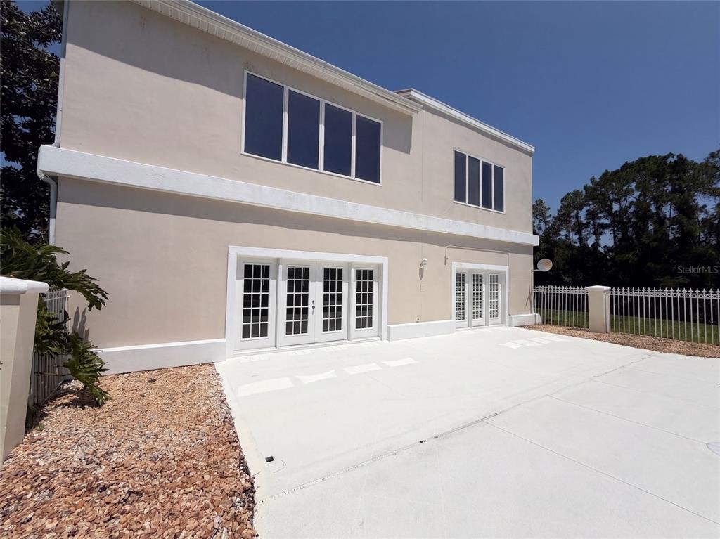 A beige two-story house exterior features a concrete patio, French doors, and large windows — 24 BAY POINTE DRIVE, ORMOND BEACH, FL