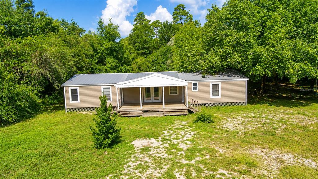 A tan mobile home with a front porch sits on a grassy lot near trees — 42135 PINE VALLEY DRIVE, PAISLEY, FL