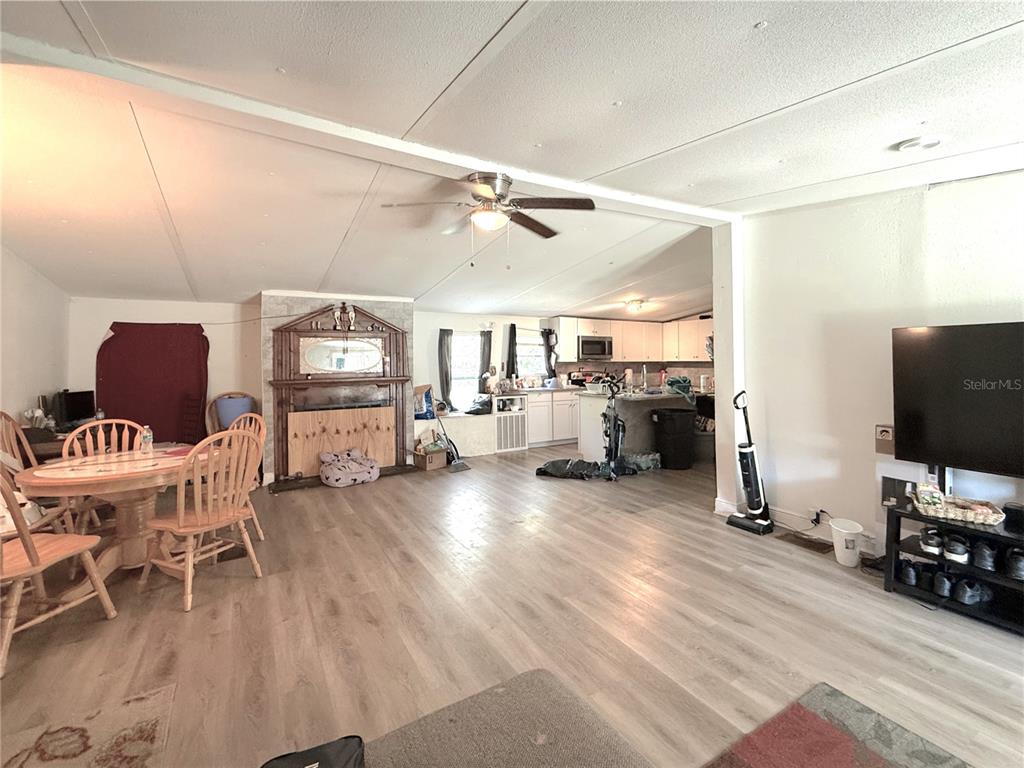An open-concept living and dining area features light wood-look flooring and a central fireplace — 42135 PINE VALLEY DRIVE, PAISLEY, FL