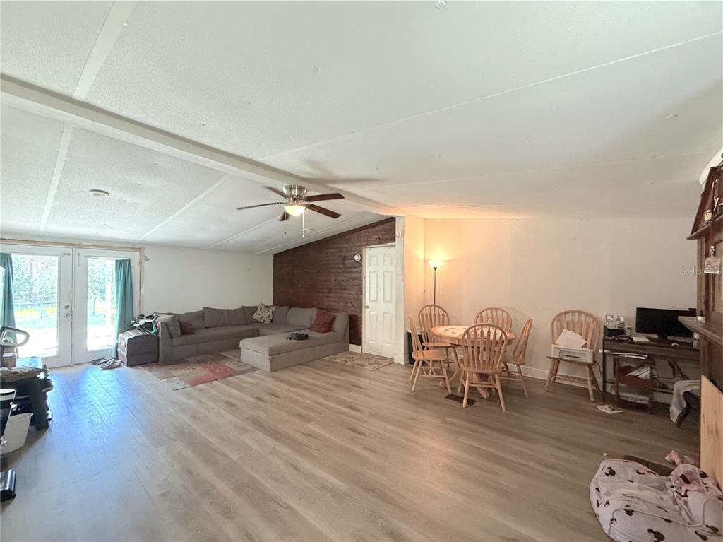A living and dining area with wood-look flooring, a sectional sofa, and a wood-paneled wall — 42135 PINE VALLEY DRIVE, PAISLEY, FL