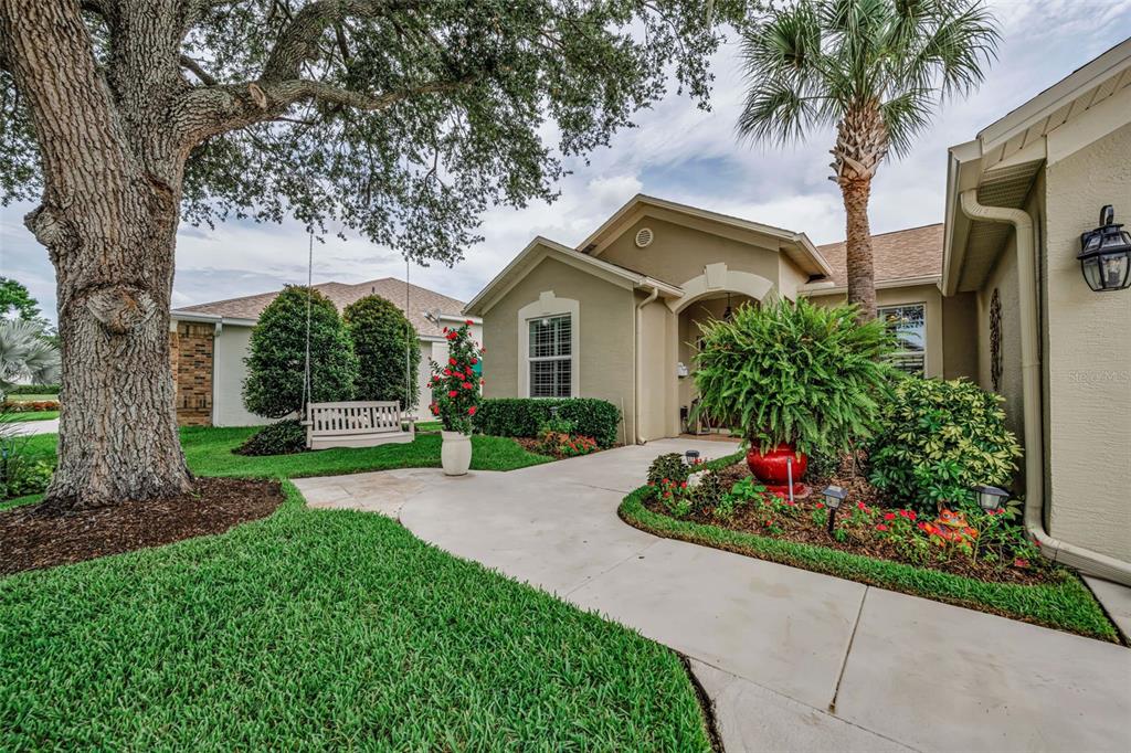 A front walkway leads to the entrance of a tan house with a porch swing — 1114 TOSKI DRIVE, TRINITY, FL