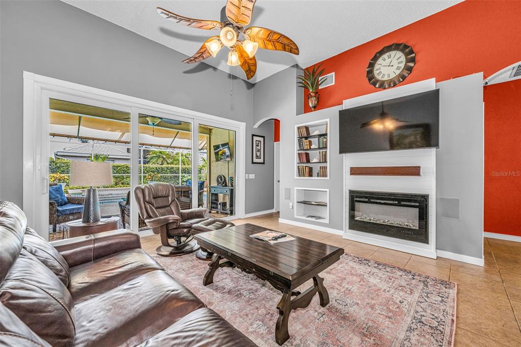 A living room features a fireplace, wall-mounted television, leather furniture, and sliding glass patio doors — 1114 TOSKI DRIVE, TRINITY, FL