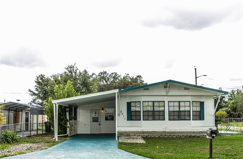 A single-story mobile home with a carport, white siding, and a blue-painted driveway — 3011 SUN WAY, LAKELAND, FL